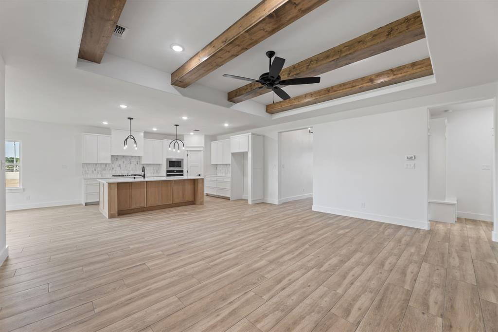 Unfurnished living room featuring ceiling fan, beamed ceiling, light wood-tile floors, and