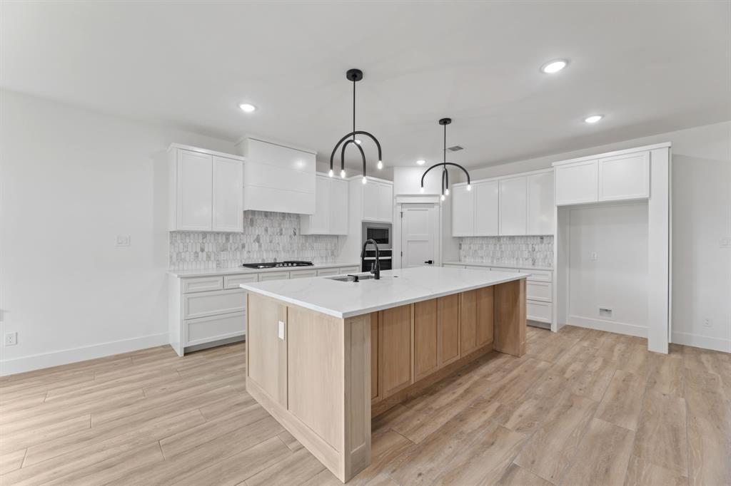 Kitchen featuring a large island with sink, a sink, appliances with stainless steel finishes, light wood-style flooring, and white cabinets