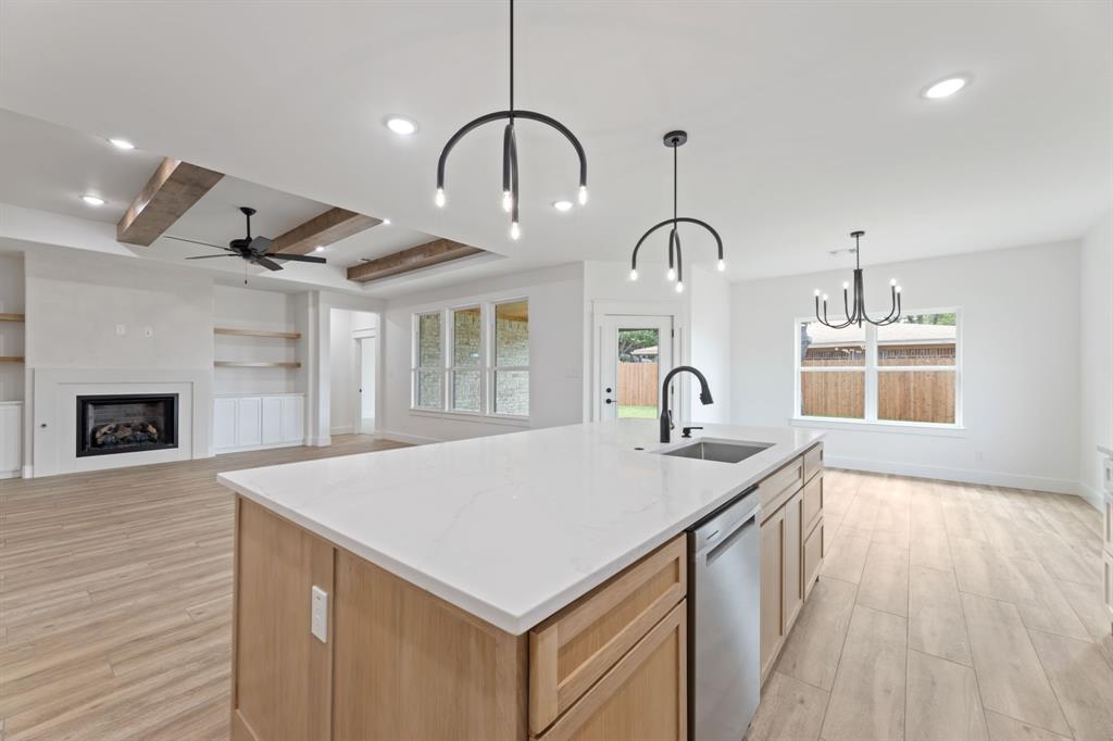 Kitchen featuring ceiling fan with notable chandelier, stainless steel dishwasher, a sink, an island with sink, and light wood-style floors