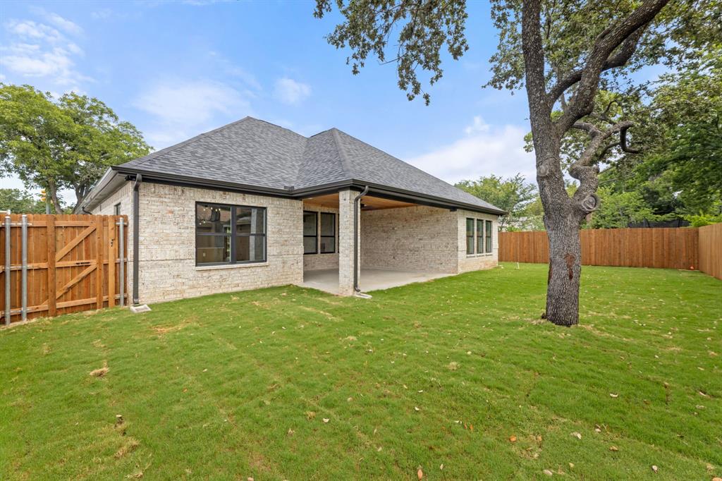 Rear view of property featuring a fenced backyard, brick siding, roof with shingles, a yard, and a patio area