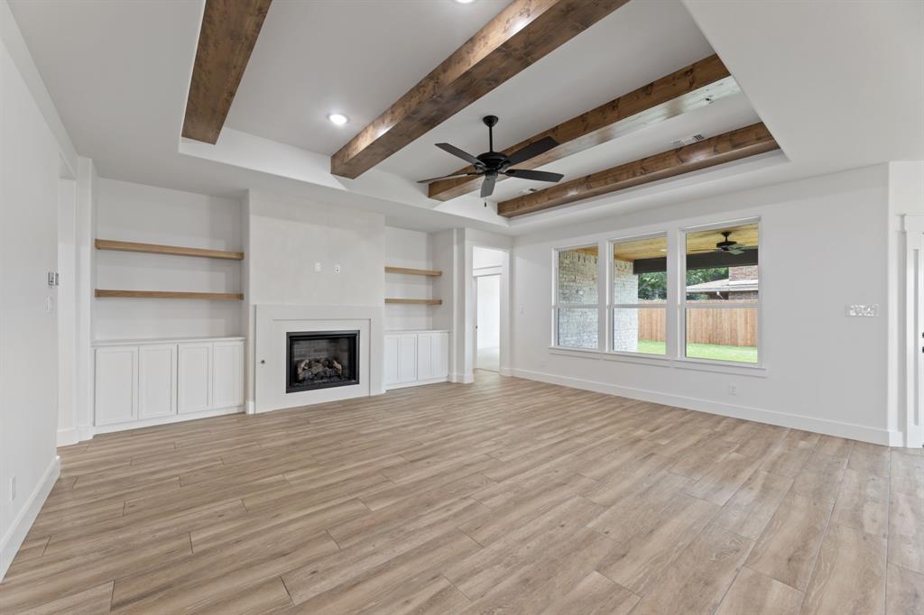 Unfurnished living room featuring light wood-style flooring, baseboards, ceiling fan, a fireplace, and beam ceiling