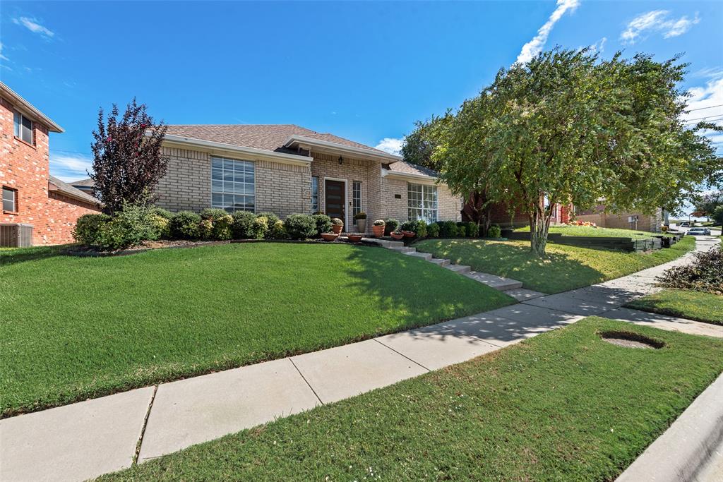 Single-story brick exterior featuring a hipped roofline, manicured lawn, and mature shade trees Single-story brick exterior featuring a hipped roofline, manicured lawn, and mature shade trees