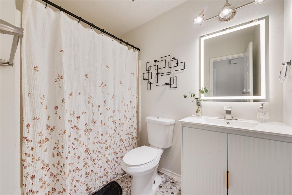 Bathroom featuring a vanity with vertical ribbed cabinet doors, a countertop with an integrated basin, a lighted mirror, and decorative wall-mounted metal shelving