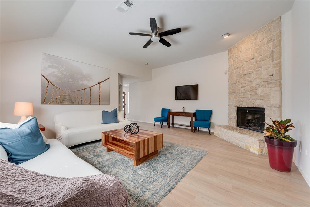 Living area featuring high ceilings, wood-finish flooring, and a full-height stone-veneer fireplace with a raised hearth Living area featuring high ceilings, wood-finish flooring, and a full-height stone-veneer fireplace with a raised hearth