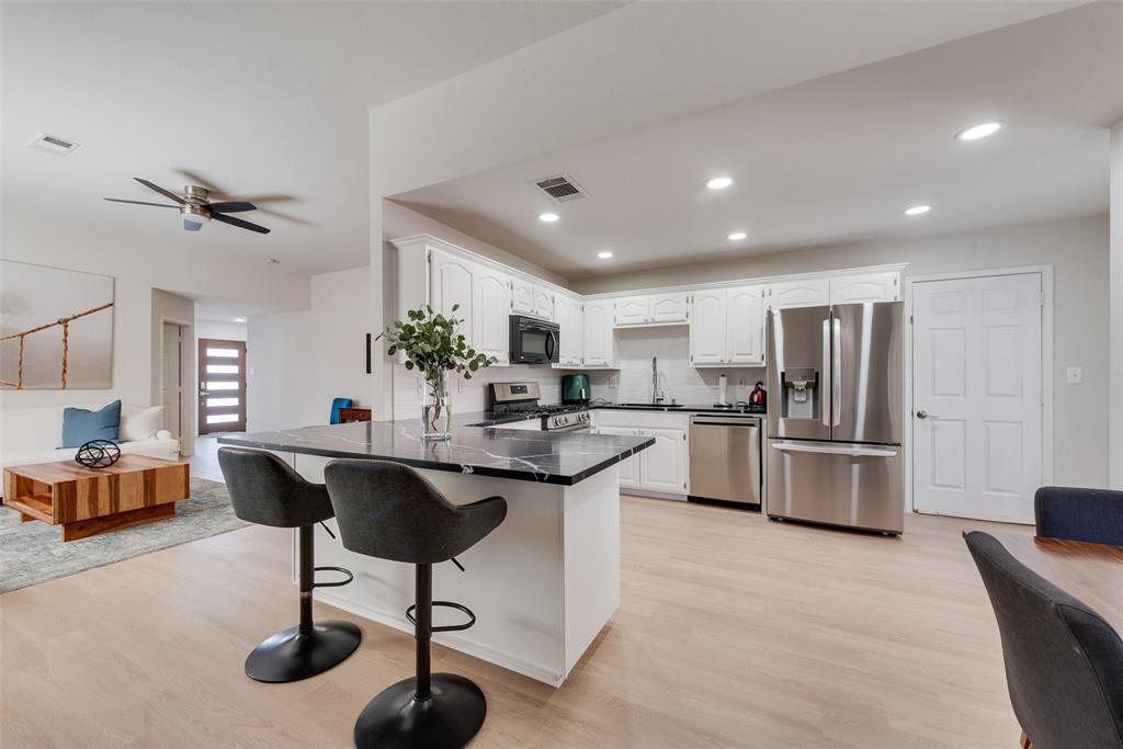 Kitchen featuring white cabinetry, dark stone-finish countertops, stainless steel appliances, a center island with a breakfast bar, and wood-finish flooring Kitchen featuring white cabinetry, dark stone-finish countertops, stainless steel appliances, a center island with a breakfast bar, and wood-finish flooring
