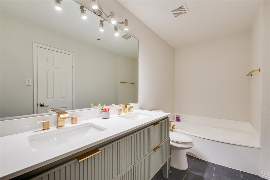Dual-sink vanity with ribbed cabinetry, white countertops, brass-finish fixtures, and a large wall-mounted mirror