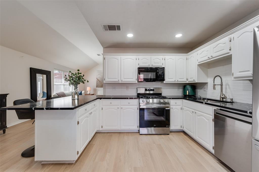 Kitchen featuring white cabinetry, dark stone-finish countertops, stainless steel appliances, and wood-finish flooring