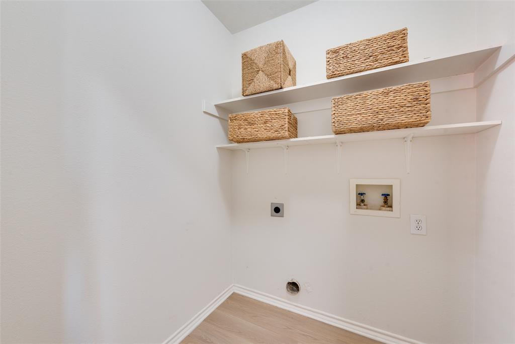Utility space featuring two tiered wall-mounted shelves, wood-finish flooring, and dedicated water and electrical hookups