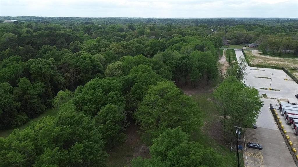 Aerial perspective of a sprawling lot featuring mature tree canopy, dense woodlands, and paved surface parking
