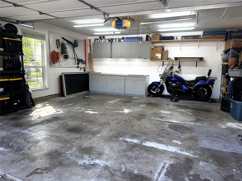 Two-car garage featuring wall-mounted upper and lower cabinetry, open shelving, fluorescent overhead lighting, and a single-pane window