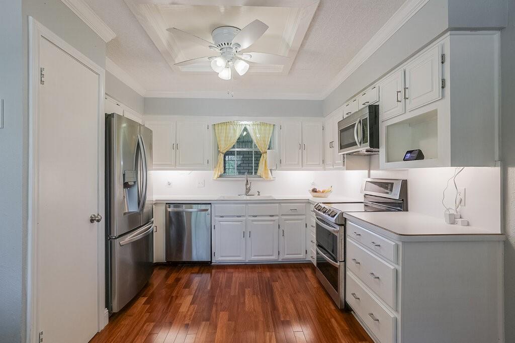 Kitchen featuring white cabinetry, wood-finish flooring, stainless steel appliances, under-cabinet lighting, and a recessed ceiling with a central fan