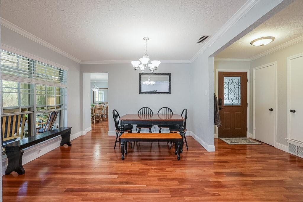 Dining area featuring wood-finish flooring, a multi-light chandelier, a built-in window bench, crown molding, and an exterior door with decorative glass inlay