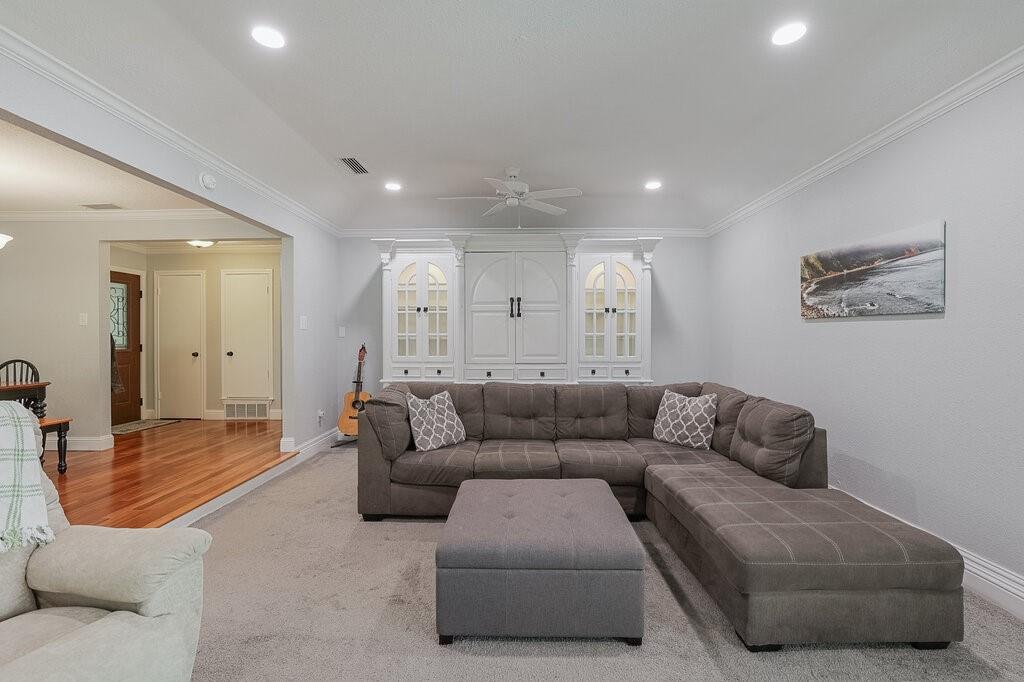 Built-in white cabinetry featuring arched glass-front display panels, recessed tray ceiling, and neutral carpeting