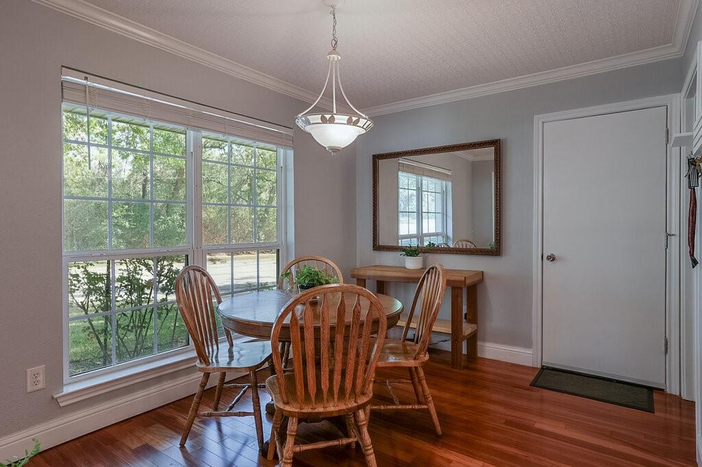Room featuring wood-finish flooring, crown molding, a multi-pane window, and a central pendant light fixture