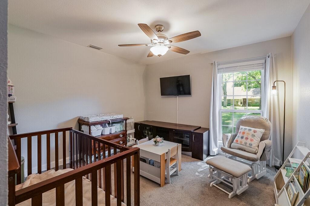 Neutral-toned bedroom featuring carpeted flooring, a multi-pane window with natural light, and a ceiling fan with integrated light fixture