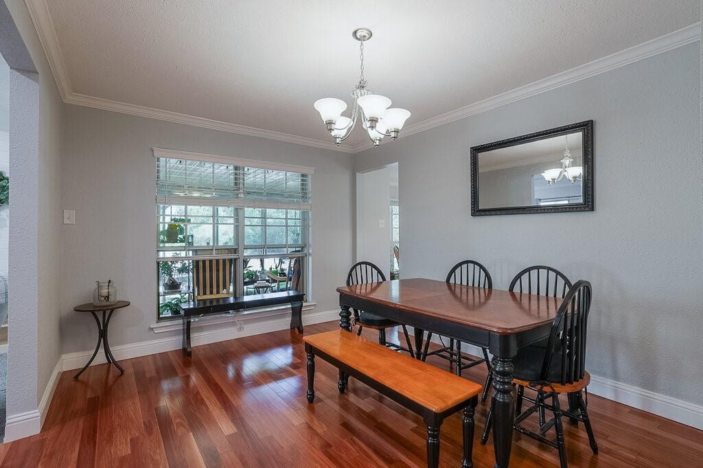 Dining area featuring wood-finish flooring, crown molding, multi-pane window, and a central five-light chandelier