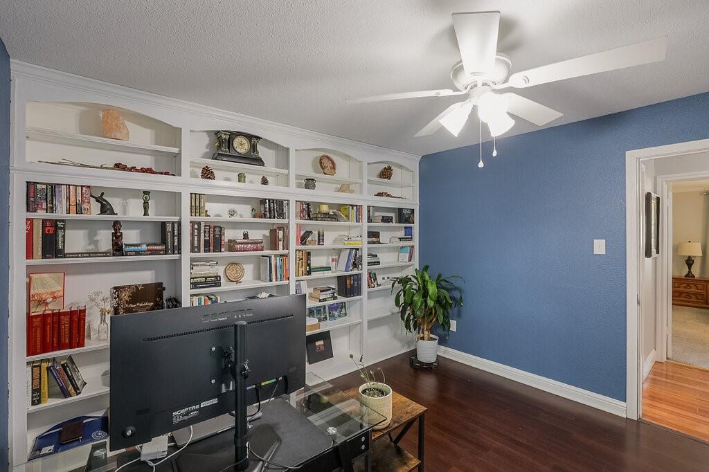 Custom floor-to-ceiling built-in white shelving, wood-finish flooring, and a multi-blade ceiling fan with integrated lighting