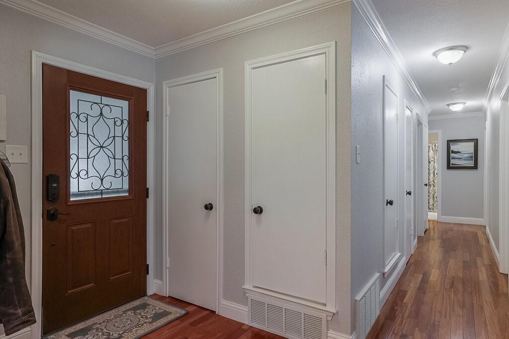 Entryway featuring a wood-finish entry door with iron detailing, wood-finish flooring, and crown molding