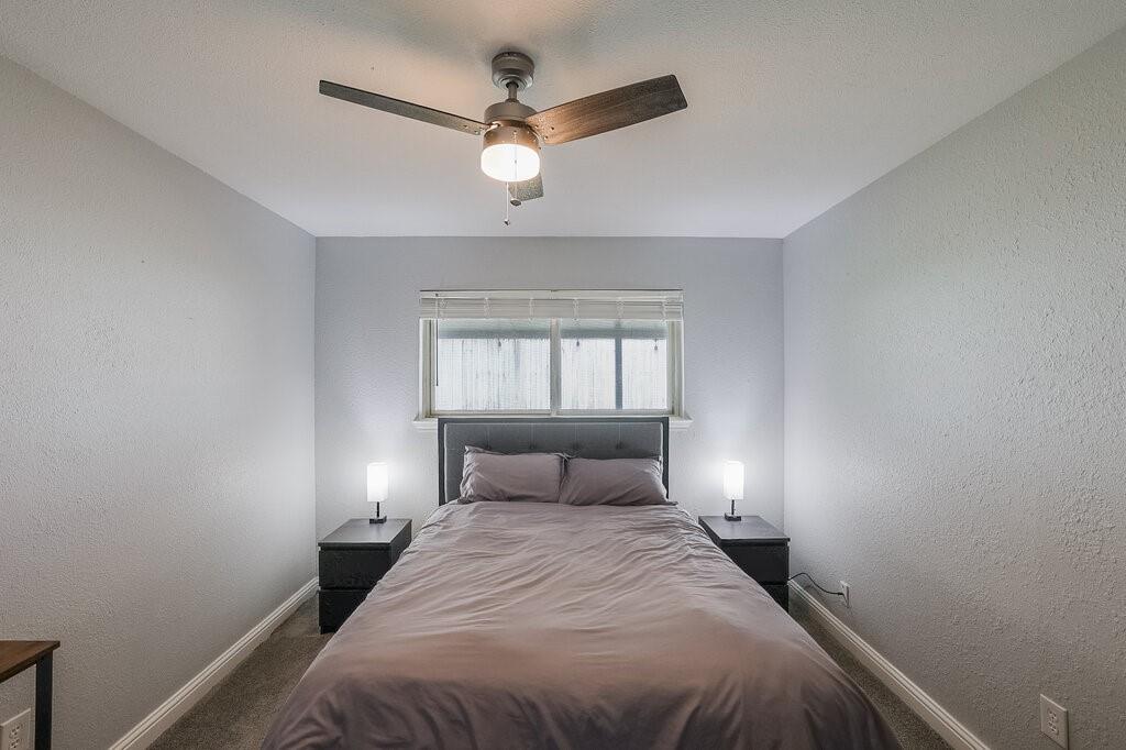 Neutral-toned interior featuring carpeting, a horizontal sliding window with blinds, and a modern ceiling fan with an integrated light fixture