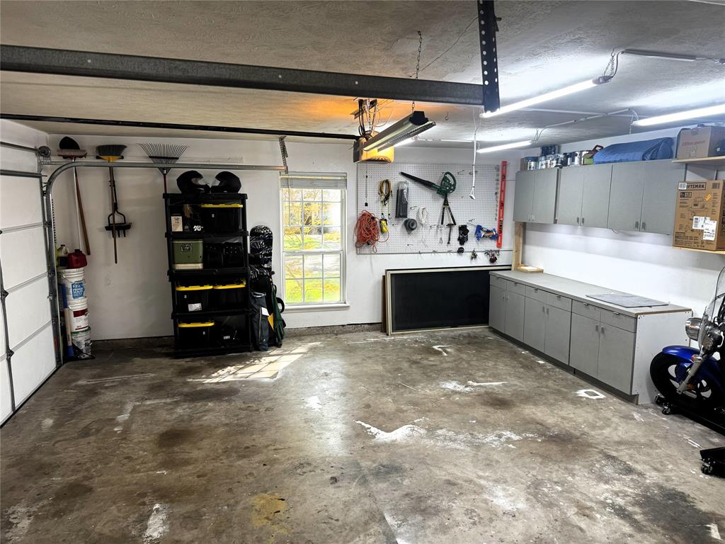 Garage space featuring concrete flooring, built-in cabinetry, dual-level wall-mounted storage units, LED lighting fixtures, and a window