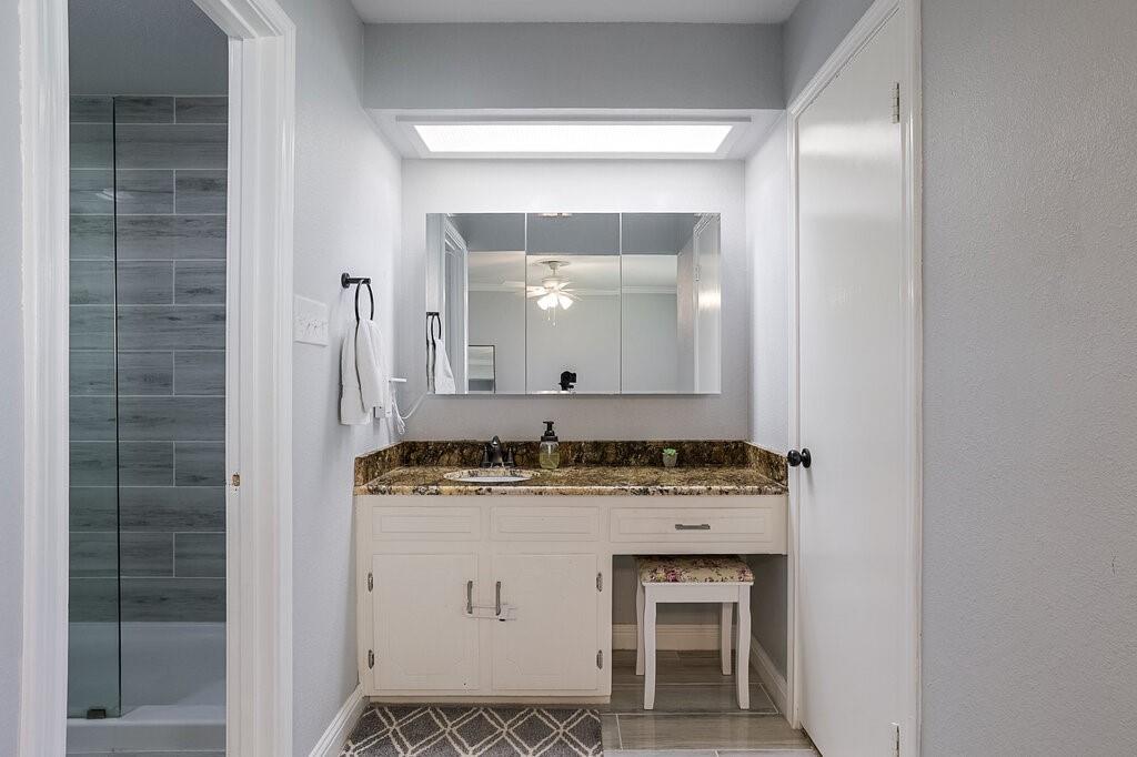 Built-in white vanity with stone-style countertop and integrated sink, recessed lighting, tri-panel medicine cabinet, and glass-enclosed shower with horizontal wall tile