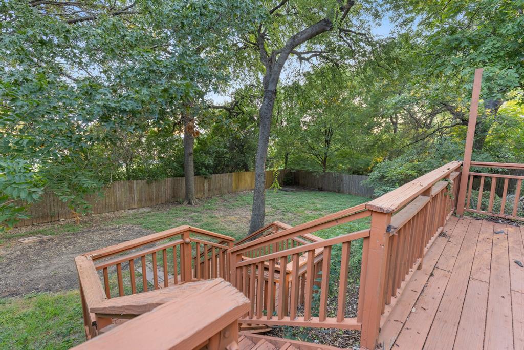 Elevated wood deck with balustrade railings, wooden staircase, mature trees, and privacy fencing