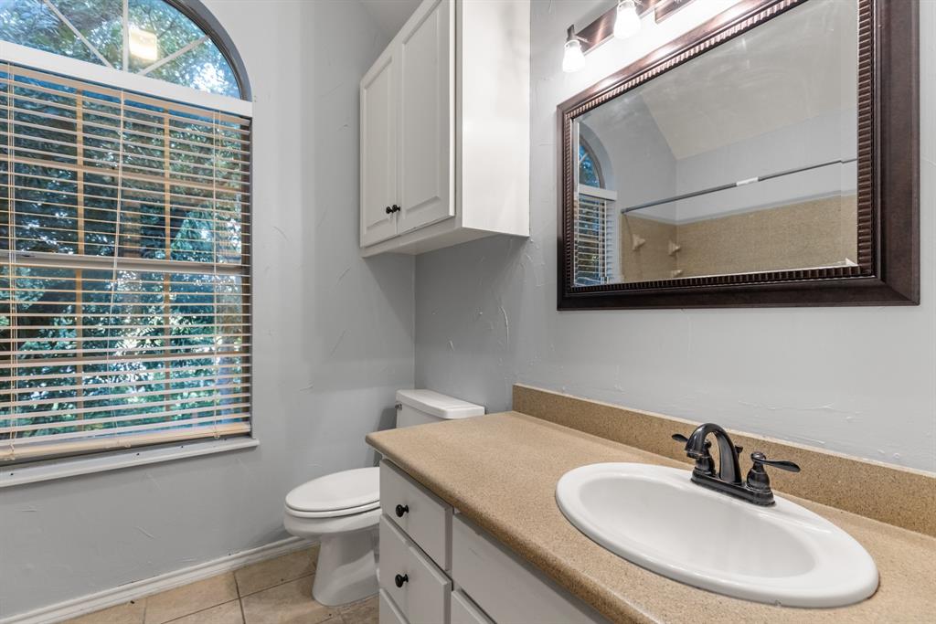 Bathroom featuring an arched window, white cabinetry with built-in wall storage, solid surface countertop with integrated oval sink, and a framed mirror