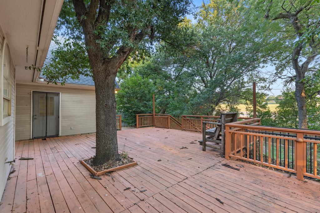 Expansive elevated wood deck featuring integrated mature tree landscaping, wooden railing with metal balusters, and stairs leading to lower-level exterior space