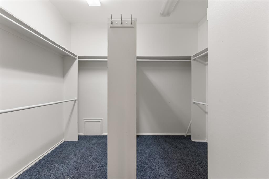 Walk-in closet featuring blue carpeting, integrated shelving units, dual hanging rods, and a central pillar equipped with wall-mounted hooks