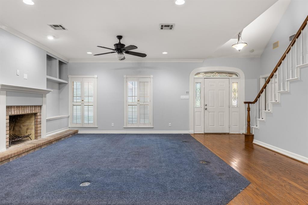 Living area featuring a masonry fireplace with a raised brick hearth, recessed ceiling lighting, built-in shelving, plantation shutters, and a staircase with a wooden handrail