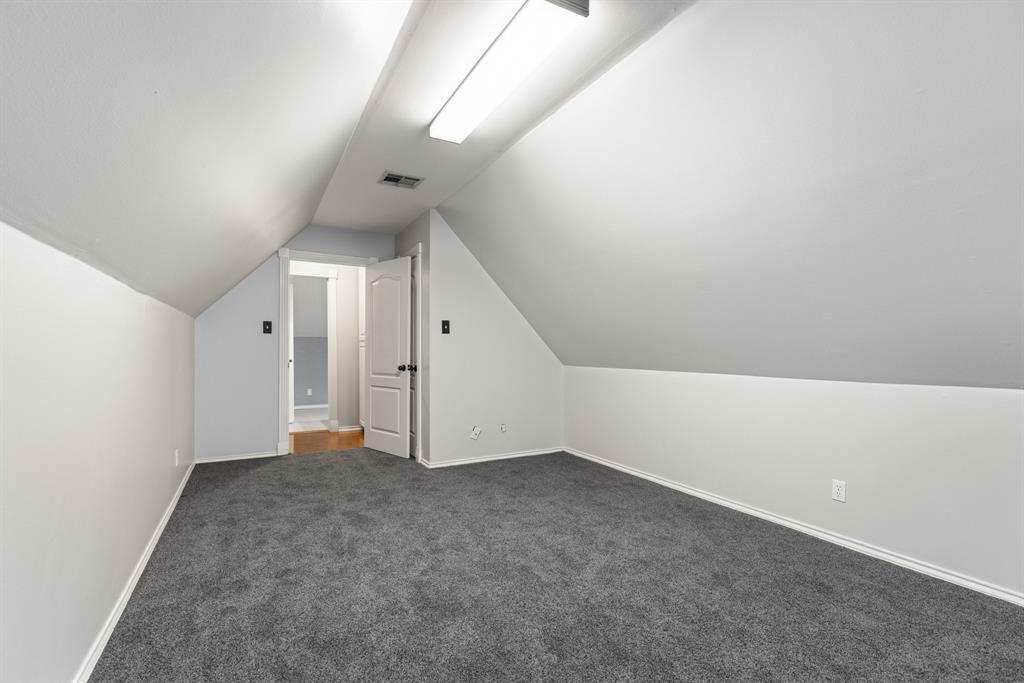 Sloped ceiling architecture featuring recessed wall angles, wall-to-wall carpeting, and a central linear light fixture