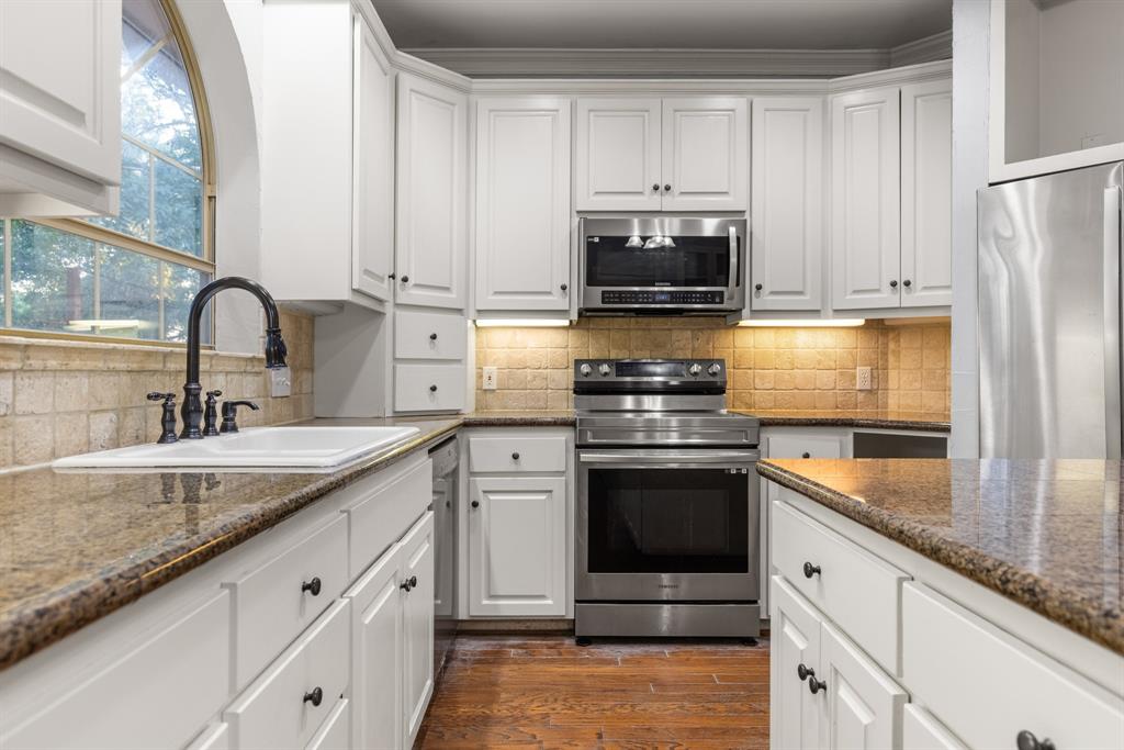Kitchen featuring white cabinetry, stone countertops, stainless steel appliances, a tile backsplash, and a farmhouse-style sink with a matte black faucet