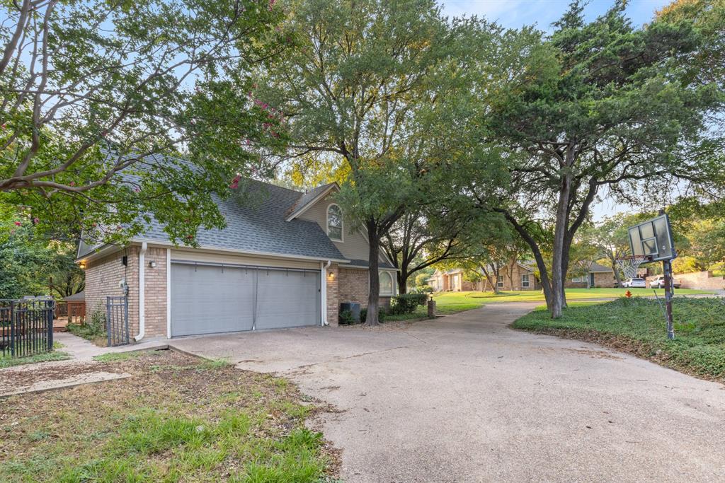 Brick exterior with a detached two-car garage, steep-pitched roofline, expansive concrete driveway, and mature landscaping