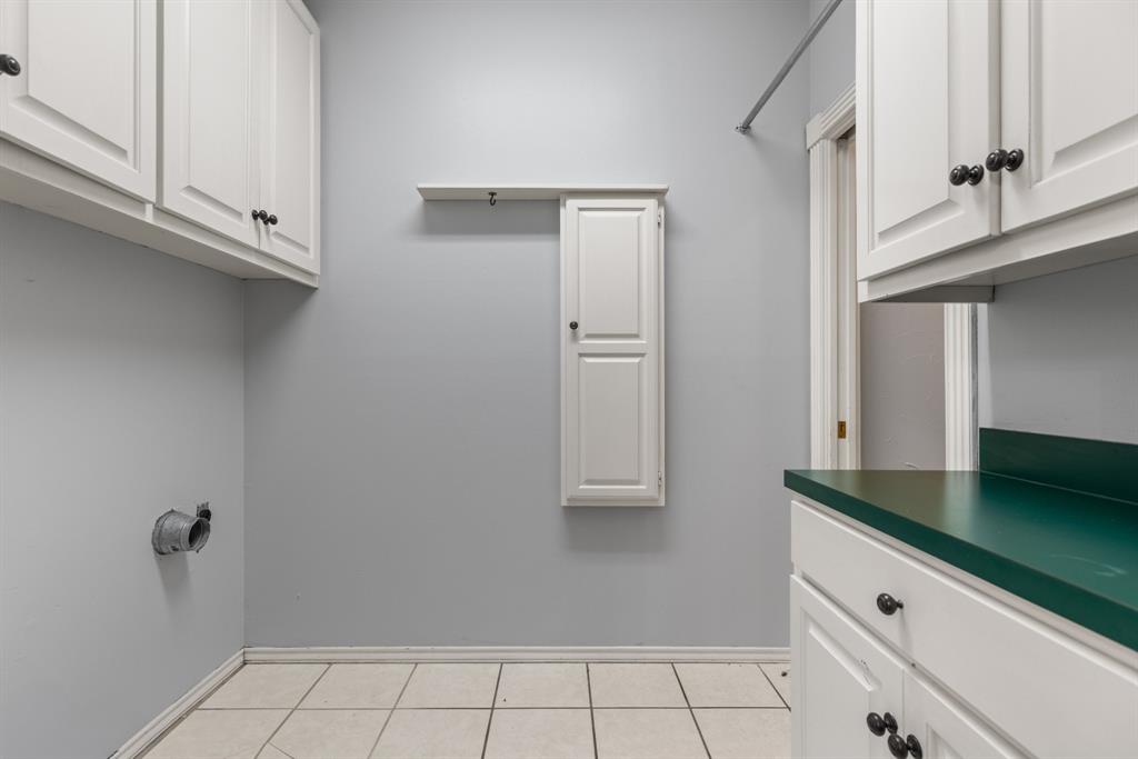 Laundry room featuring white cabinetry, a wall-mounted storage cabinet with a shelf, a metal hanging rod, and tile flooring