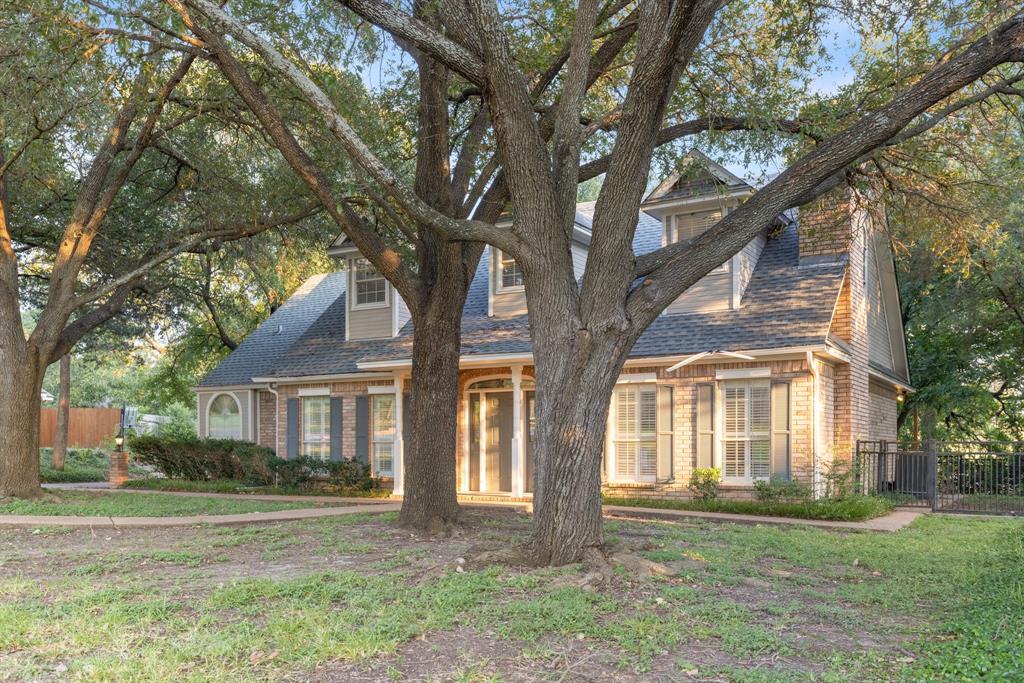 Two-story brick exterior featuring a multi-gabled roofline, dormer windows, shutters, and mature trees
