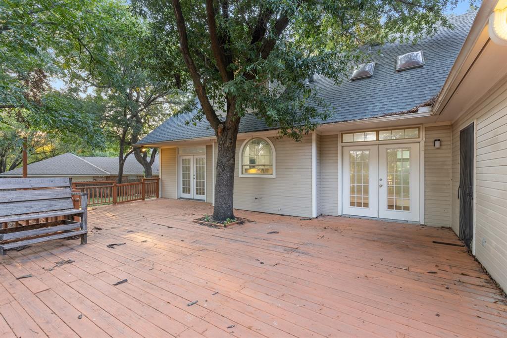 Expansive wooden deck featuring built-in seating, dual sets of French doors, an integrated mature tree, and roof-mounted skylights