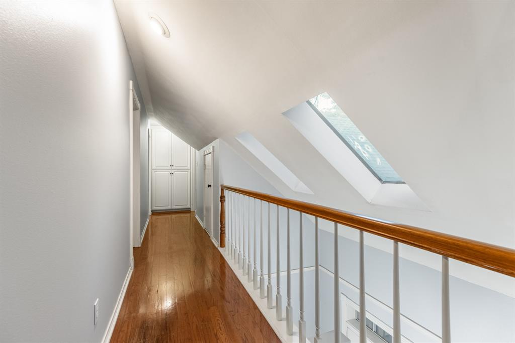 Hallway featuring wood-finish flooring, vaulted ceilings, dual skylights, built-in cabinetry, and a wooden handrail with painted balusters