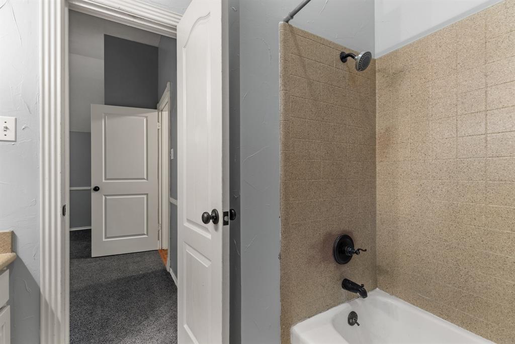 Bathroom featuring a shower and tub combination with matte black fixtures, textured tile surround, and arched-panel interior doors