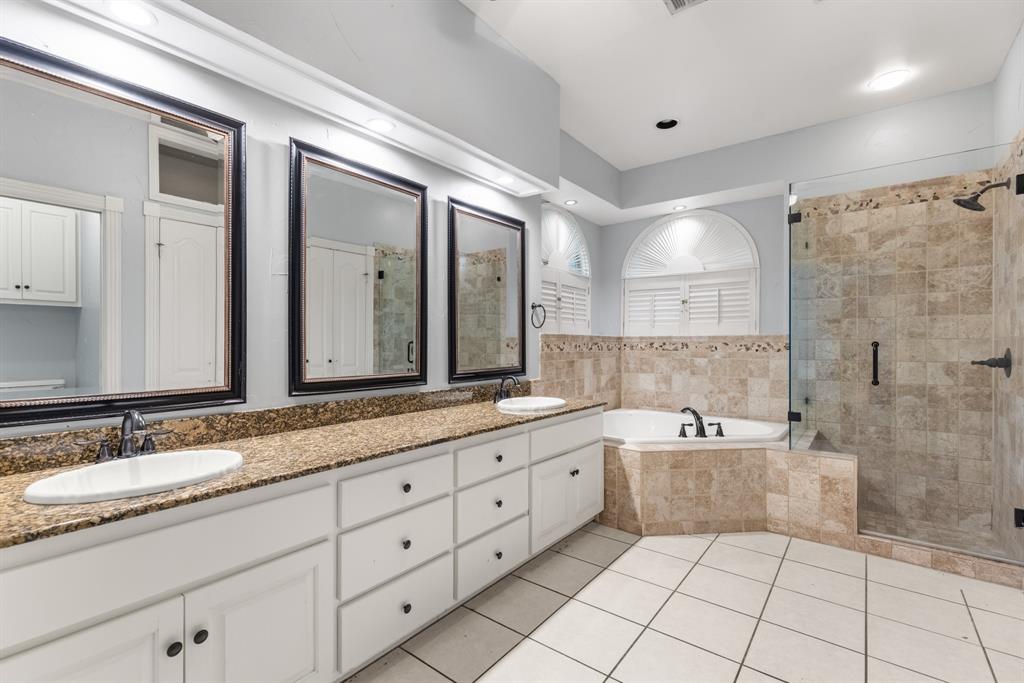 Dual vanity with white cabinetry and stone countertops, oversized framed wall mirrors, corner soaking tub with tile surround, and walk-in glass-enclosed shower