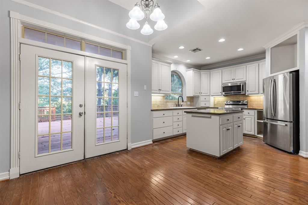 Kitchen featuring white cabinetry, center island with stone countertop, stainless steel appliances, wood-finish flooring, and French doors with transom windows