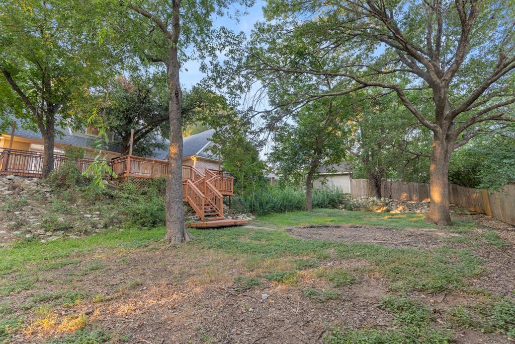 Multi-level wood deck with stairs, stone retaining wall, and mature trees on a spacious lot