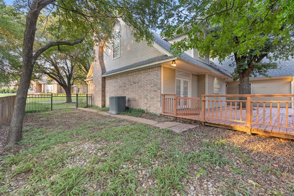 Exterior featuring a brick and siding facade, raised wood deck with railing, metal perimeter fencing, and mature trees