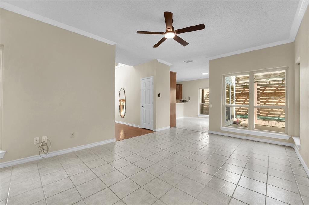 Neutral-toned interior featuring ceramic tile flooring, a central ceiling fan with integrated lighting, expansive window sets, crown molding, and a multi-panel interior door