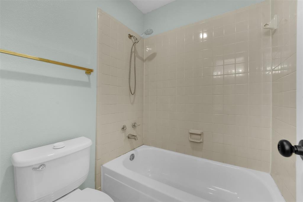 Full bathtub enclosure featuring glossy ceramic wall tile, a handheld shower fixture, built-in soap dish, and a wall-mounted gold-finish towel bar