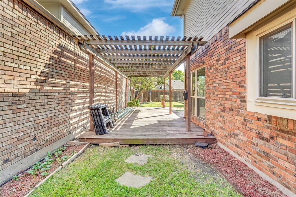 Outdoor area featuring a wooden deck with a built-in pergola, flanked by brick exterior walls and a small grass lawn