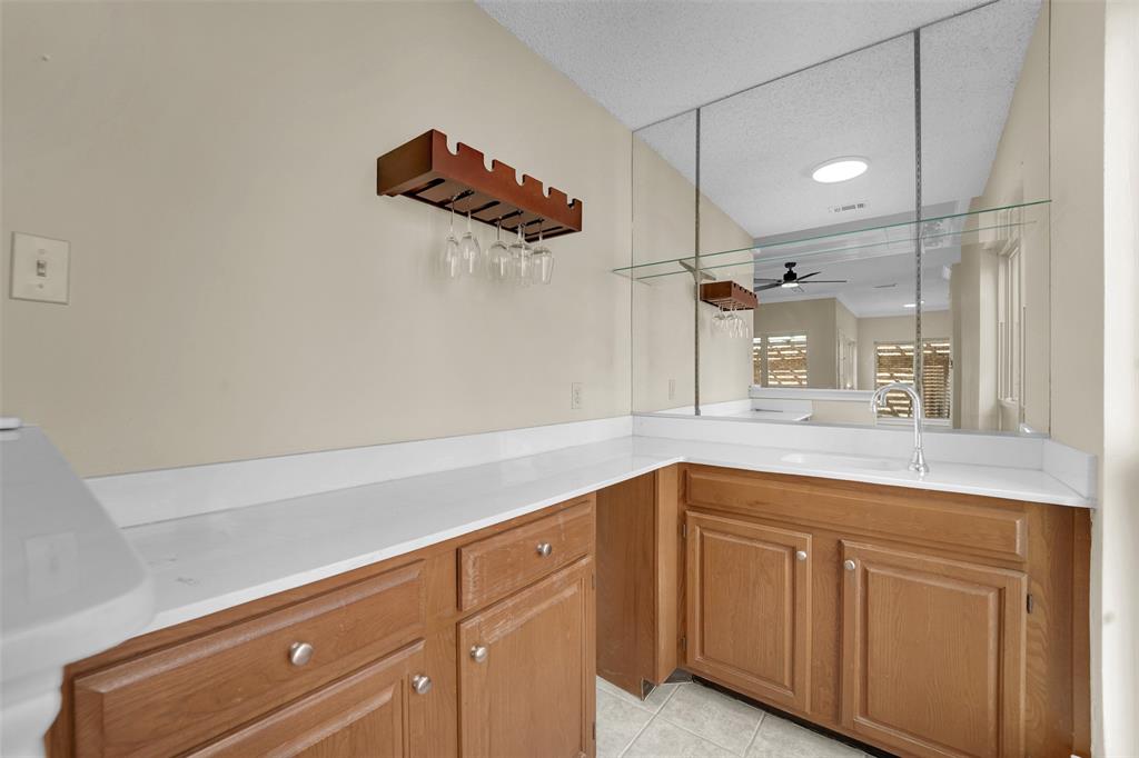 Wet bar featuring wood-finish cabinetry, solid-surface countertops, a stainless steel gooseneck faucet, integrated sink, and full-height mirrored backsplash