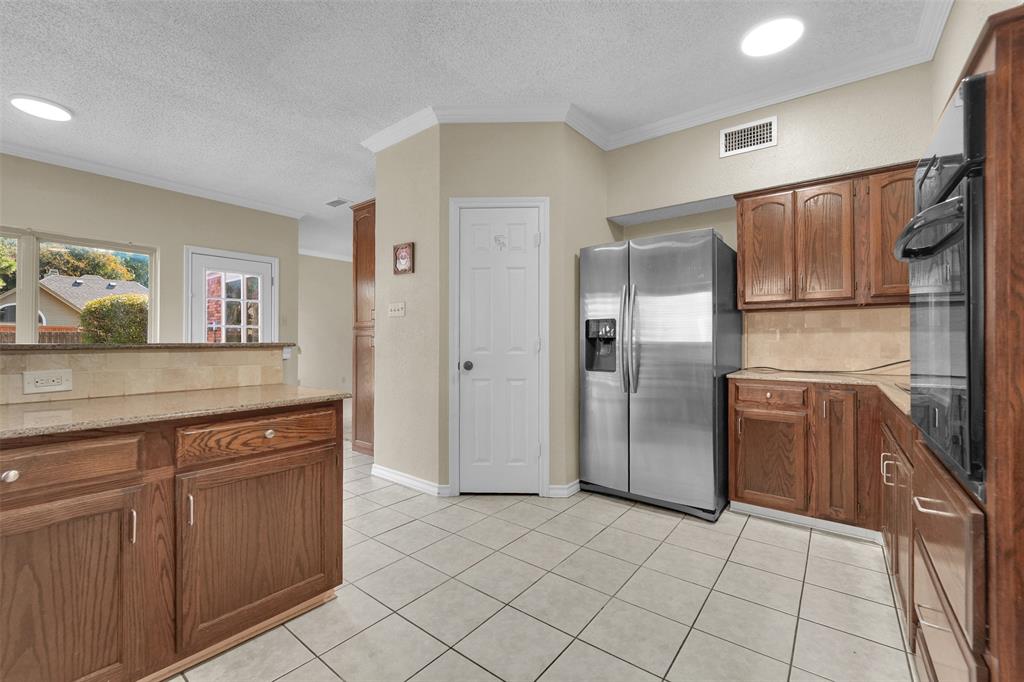 Kitchen featuring wood cabinetry, stone countertops, tiled backsplash, stainless steel refrigerator, and built-in wall oven
