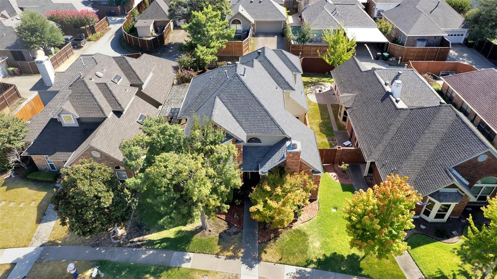 Aerial perspective of a multi-gabled roofline featuring asphalt shingles, light-toned exterior masonry, mature trees, and a concrete front walkway