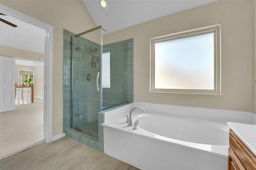 Bathroom featuring a soaking tub, a glass-enclosed shower with tiled walls and a built-in recessed niche, and wood-finish flooring