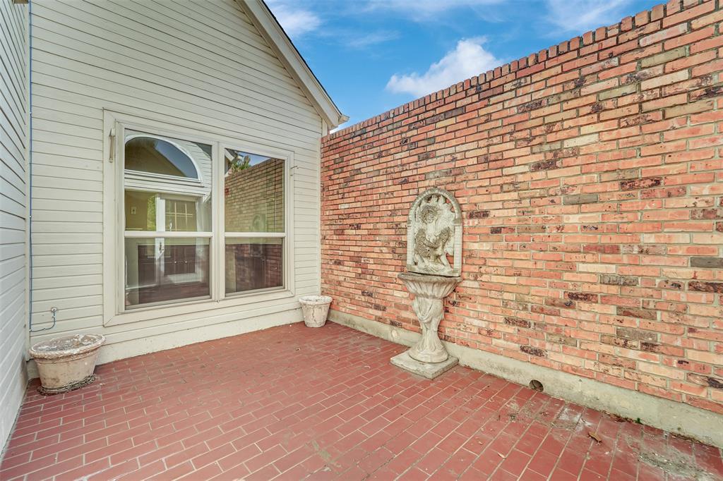 Enclosed courtyard featuring red brick masonry flooring, a perimeter brick wall, a built-in stone fountain, and horizontal siding exterior